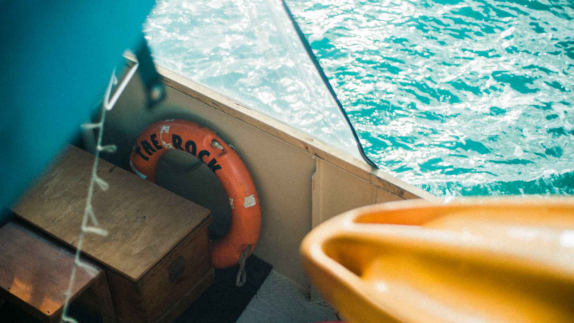 An onboard view of The Rock - a kayak, life ring branded 'The Rock', and turquoise water alongside the hull
