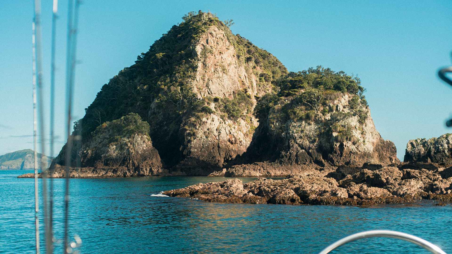 Rugged rocky island rising from turquoise water in the Bay of Islands, viewed from the boat